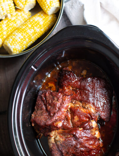 Cooked barbecue ribs in the slow cooker with corn on the cob on the side.