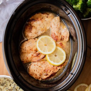 5 chicken breasts in a slow cooker with lemons on top.