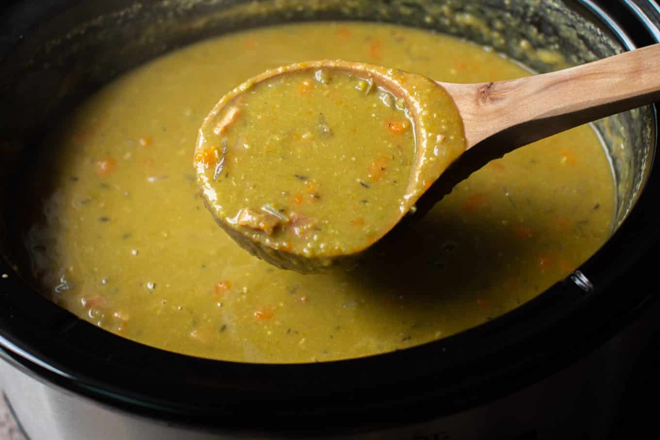 ladle of split pea soup coming from the slow cooker.