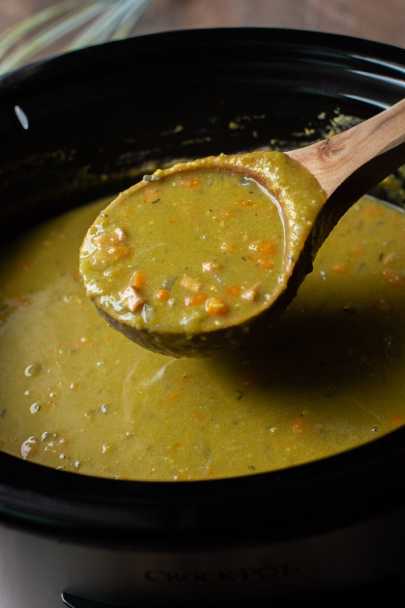 ladle full of split pea soup coming from the slow cooker.