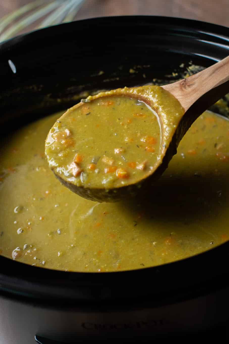 close up of bright green split pea soup on a ladle coming from slow cooker.