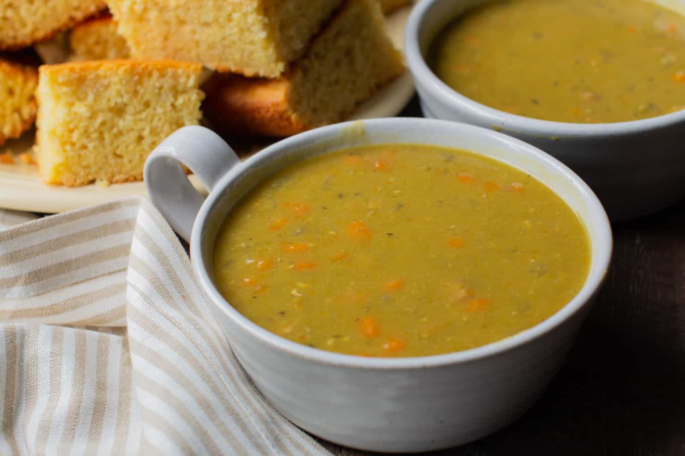 bowls of split pea soup with cornbread in the background.