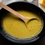 bright green split pea soup in a slow cooker with a wooden spoon in it.