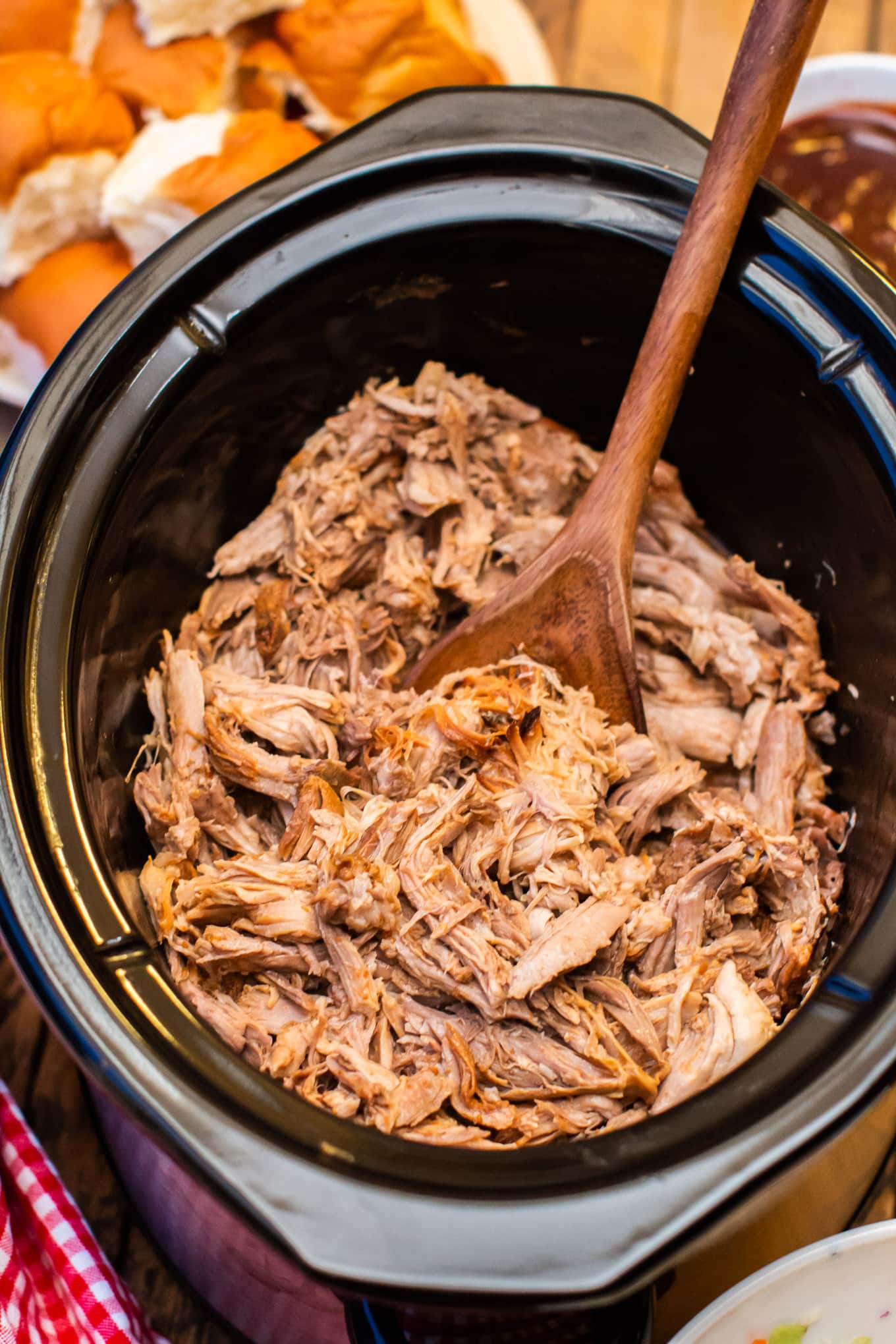 Shredded pulled pork with buns and barbecue sauce on side.
