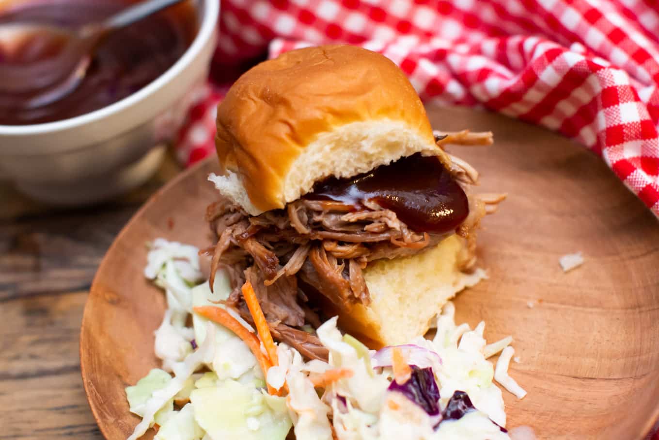 pulled pork sandwich topped with barbecue sauce and coleslaw on the side