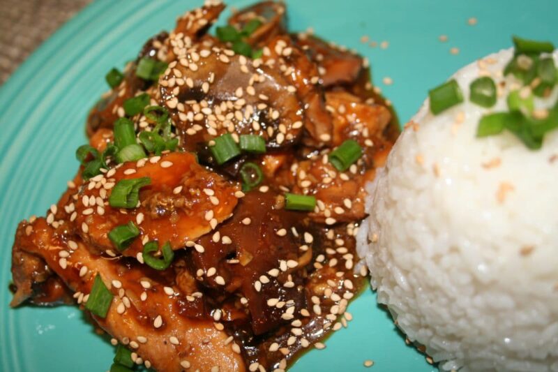 sesame chicken with sesame seeds and green onion on top with rice on the side.