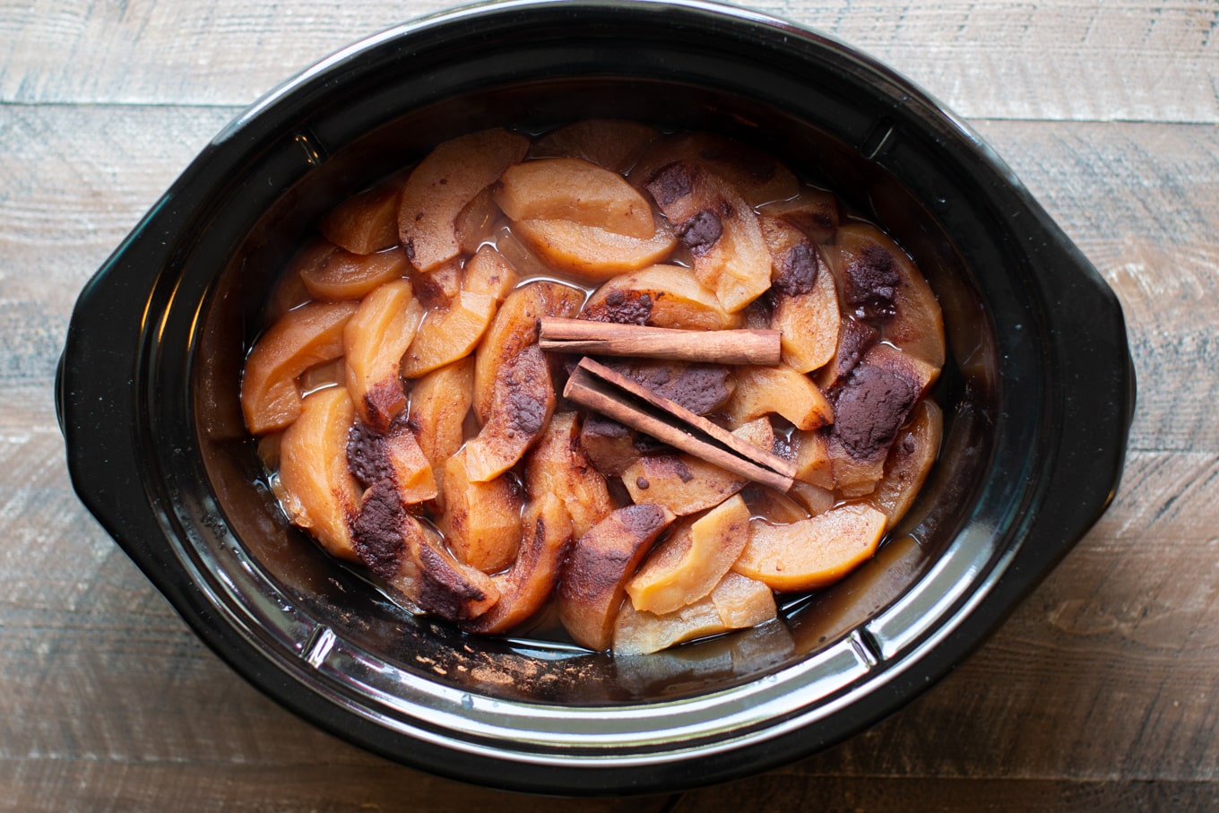 Cooked apples in a slow cooker with cinnamon on top.