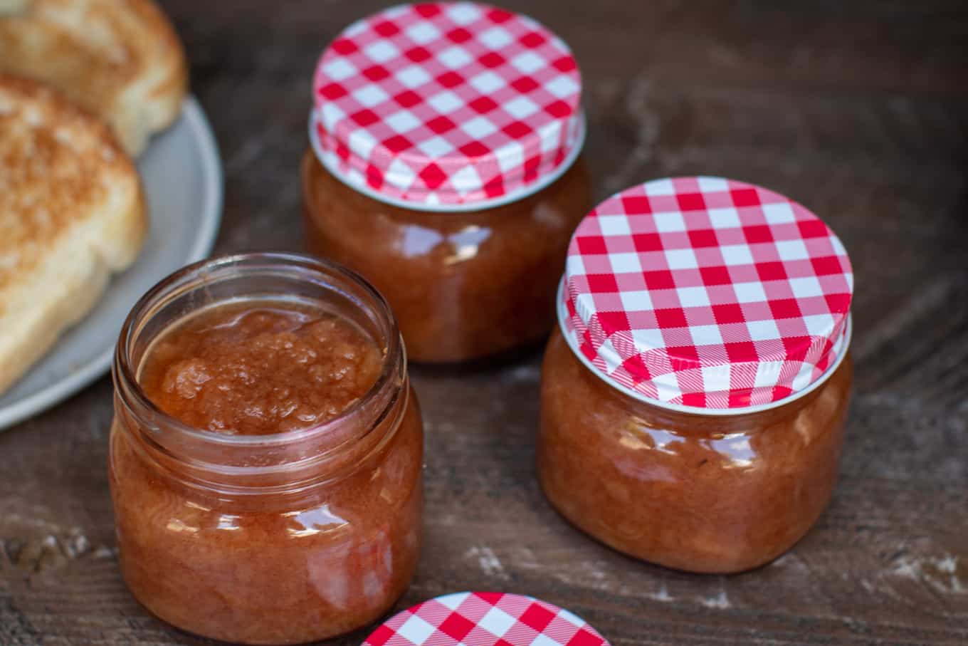 3 jars of apple sauce on a wooden table.