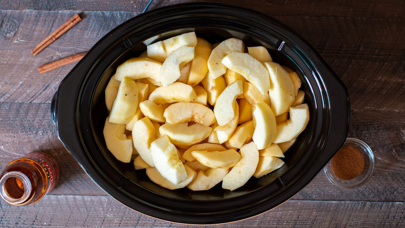 Sliced and peeled apples in a large slow cooker.