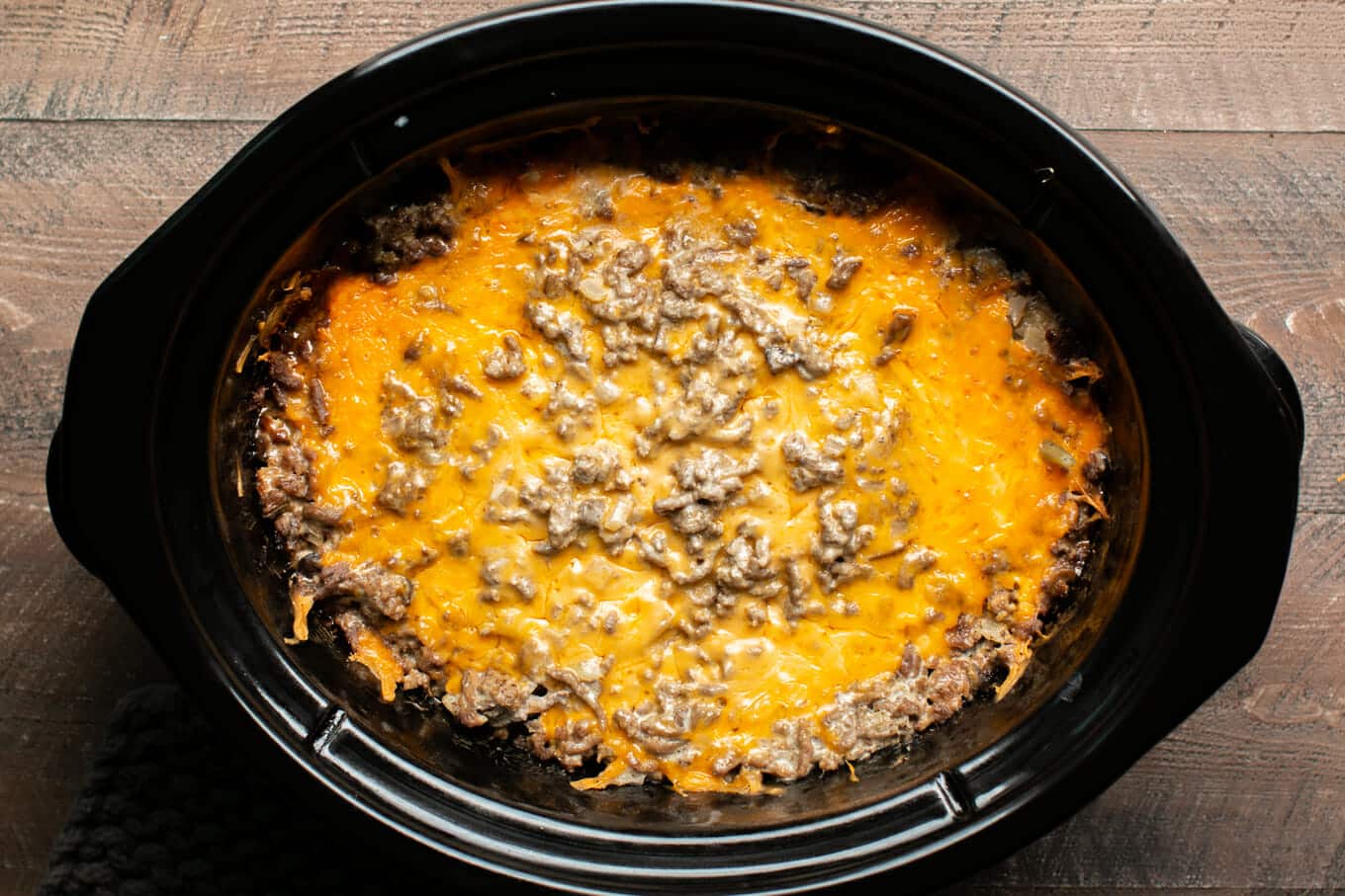 Cooked tater tot casserole in slow cooker with cheese on top.
