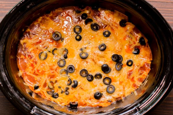 enchilada casserole in slow cooker with cheese and olives on top.