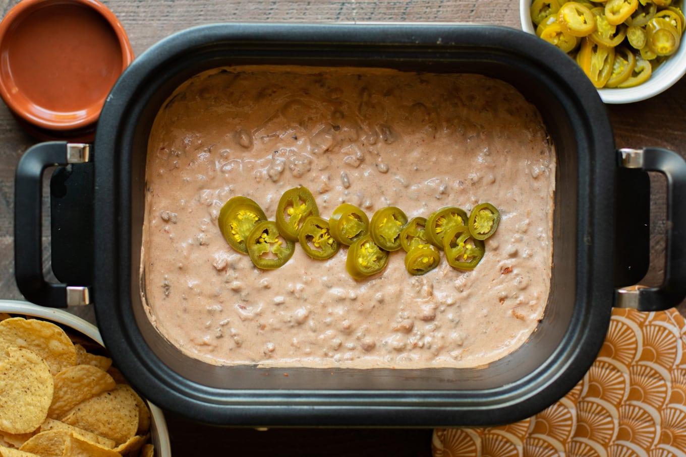 Taco dip in slow cooker with jalapenos on top, chips on the side.