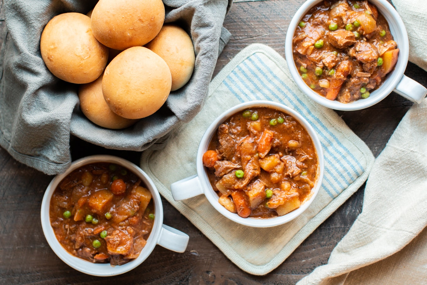 3 bowls of beef stew in white bowls with rolls on side