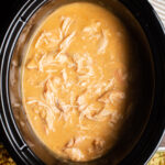 Slow Cooker with chicken gravy and shredded chicken in it.