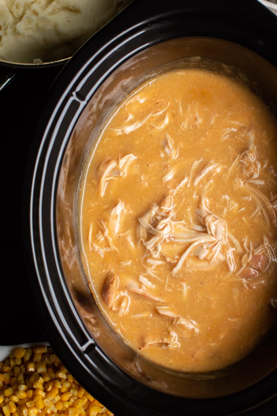 Golden colored gravy with shredded chicken in it, in a slow cooker.