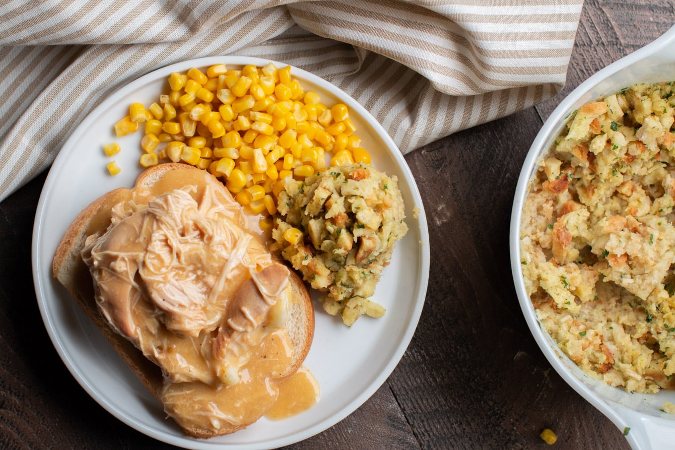 Plate of bread, mashed potatoes and chicken and gravy on top. Corn and stuffing on the side.