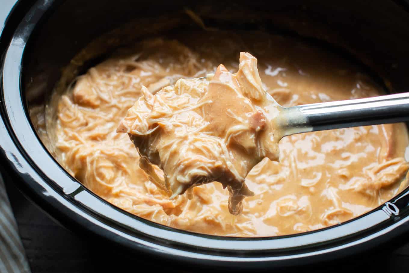 shredded chicken in gravy on a spoon coming from slow cooker.