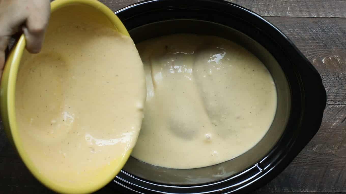Gravy mixture being poured over chicken breasts in a slow cooker.