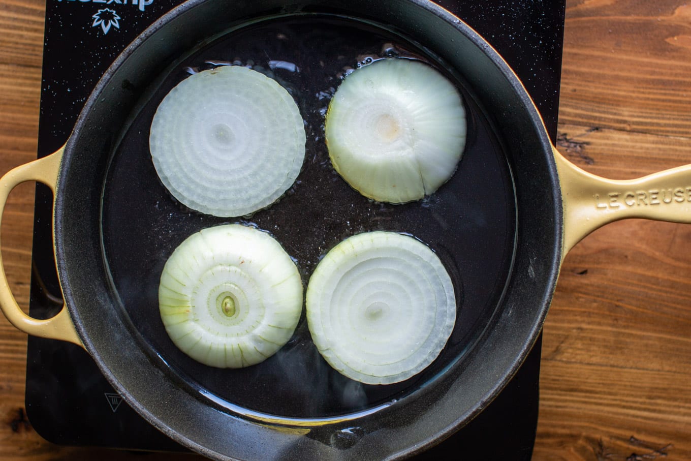 4 slices of yellow onion frying in a cast iron pan.