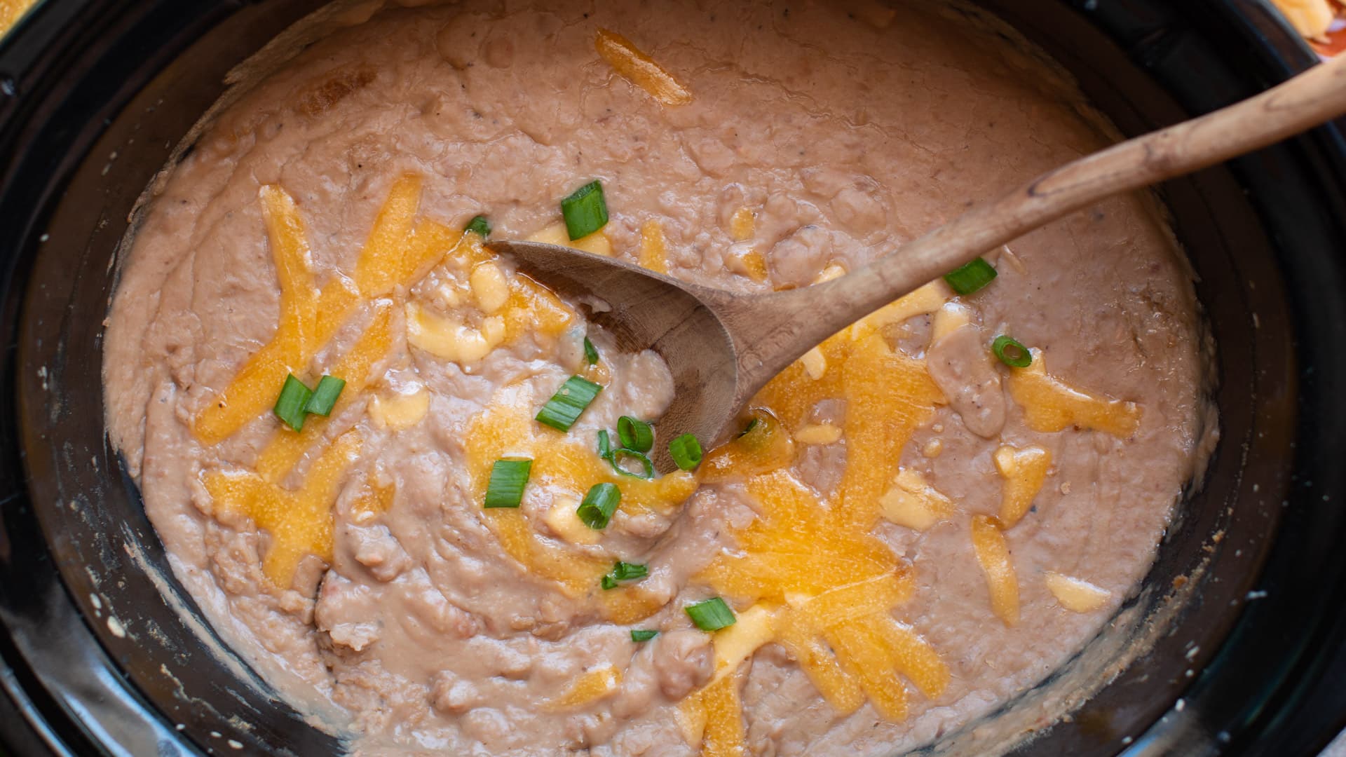 creamy refried beans in a slow cooker with cheese and green onion on top.