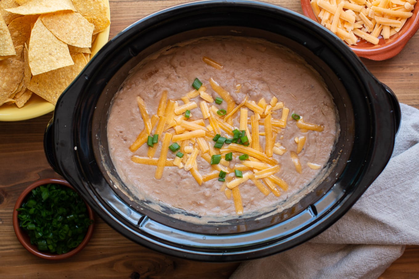 pureed pinto beans in a slow cooker with chips and cheese on the side.