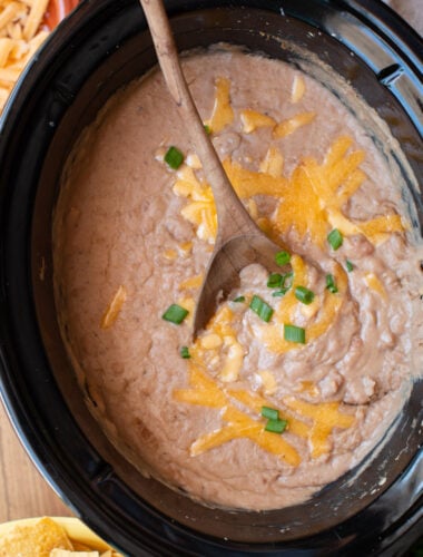 refried beans in a slow cooker with a wooden spoon in it.