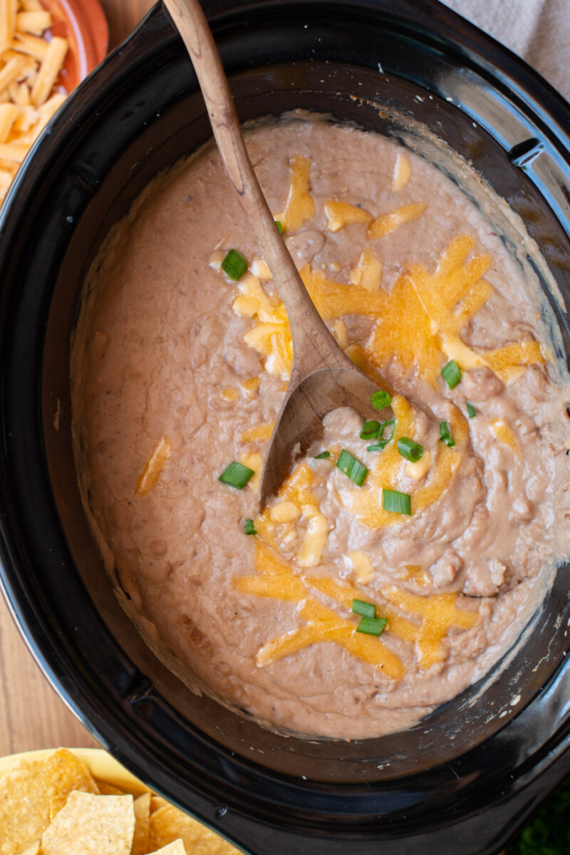 refried beans in a slow cooker with a wooden spoon in it.