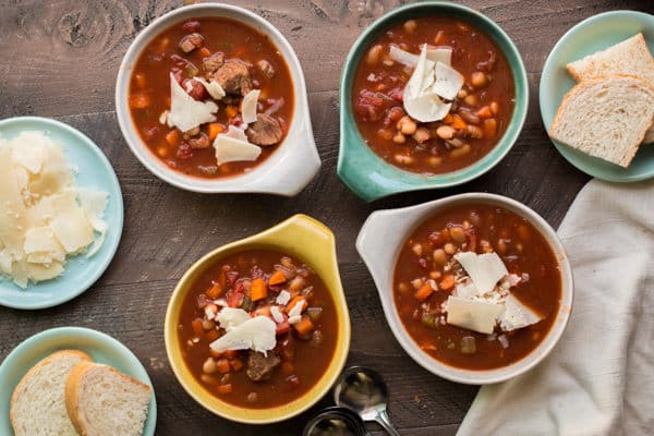 4 multi colored bowls of hearty Italian beef soup with parmesan on top.