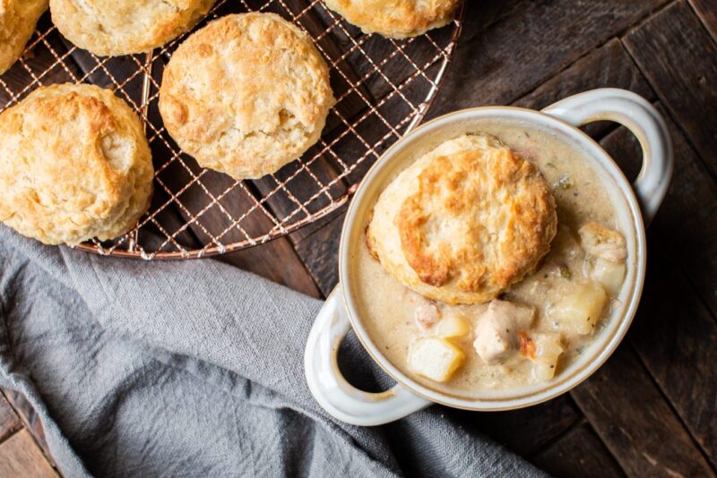 chicken pot pie filling in bowl with biscuit on top, grey napkin next to it