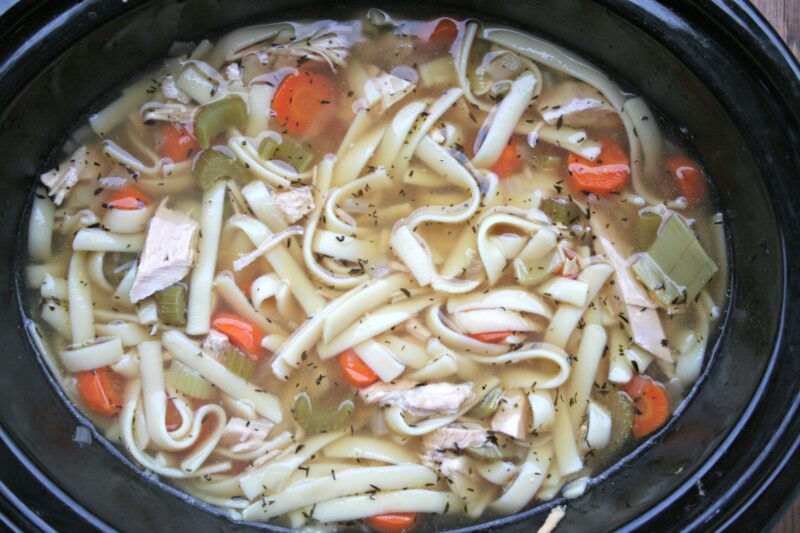 closeup photo of turkey noodle soup with carrots, and celery in a slow cooker