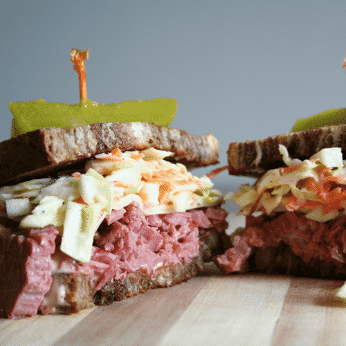 Reuben Sandwich with homemade Russian dressing cut in half on cutting board