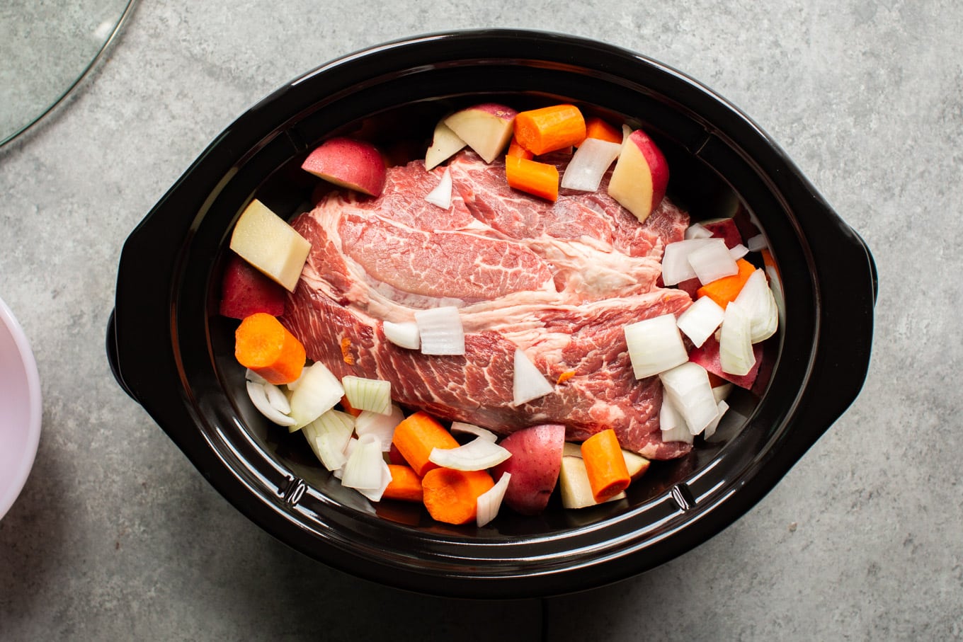 raw pot roast with carrots, potatoes and onion on the top.