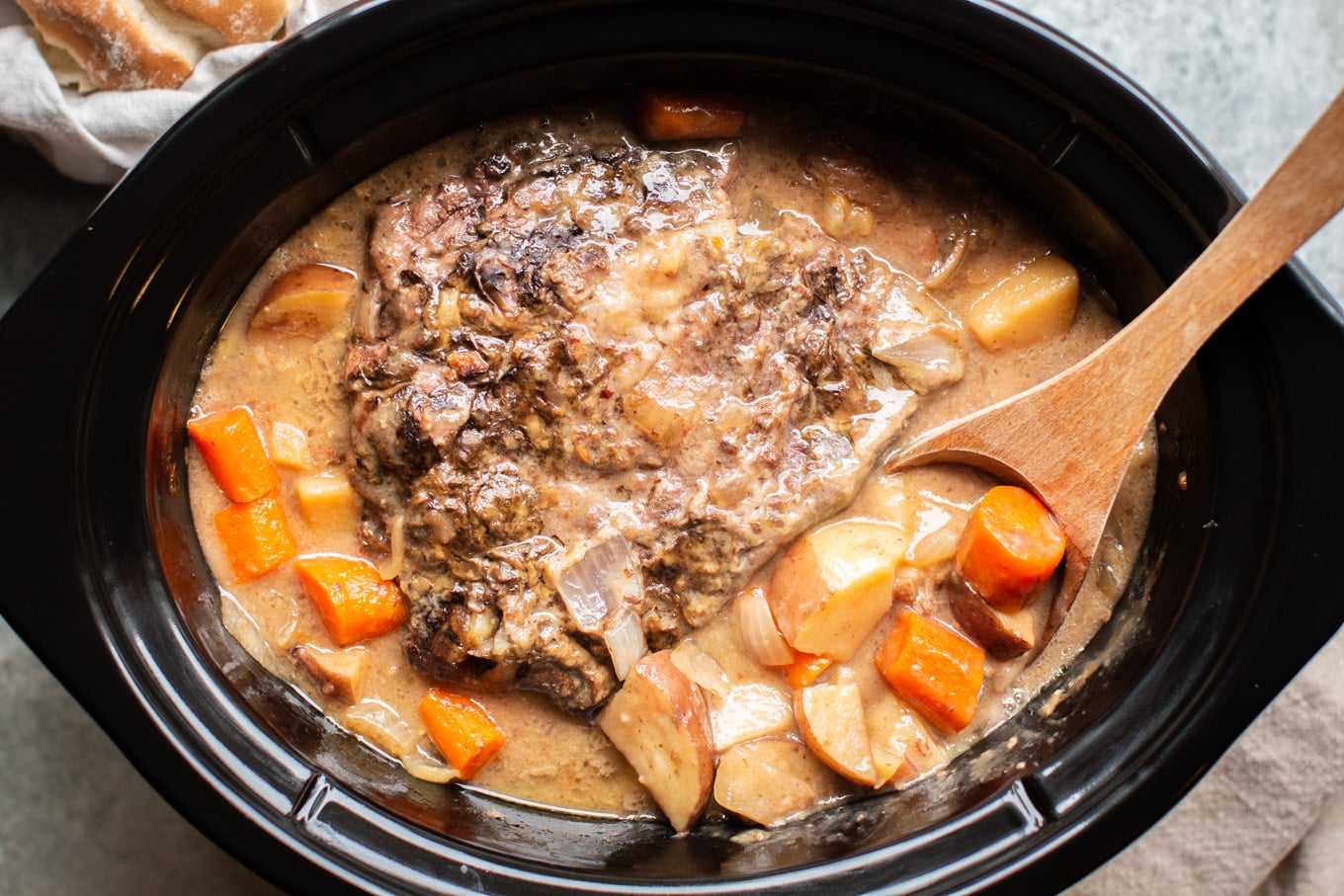 cooked pot roast in gravy with vegetables in a slow cooker.