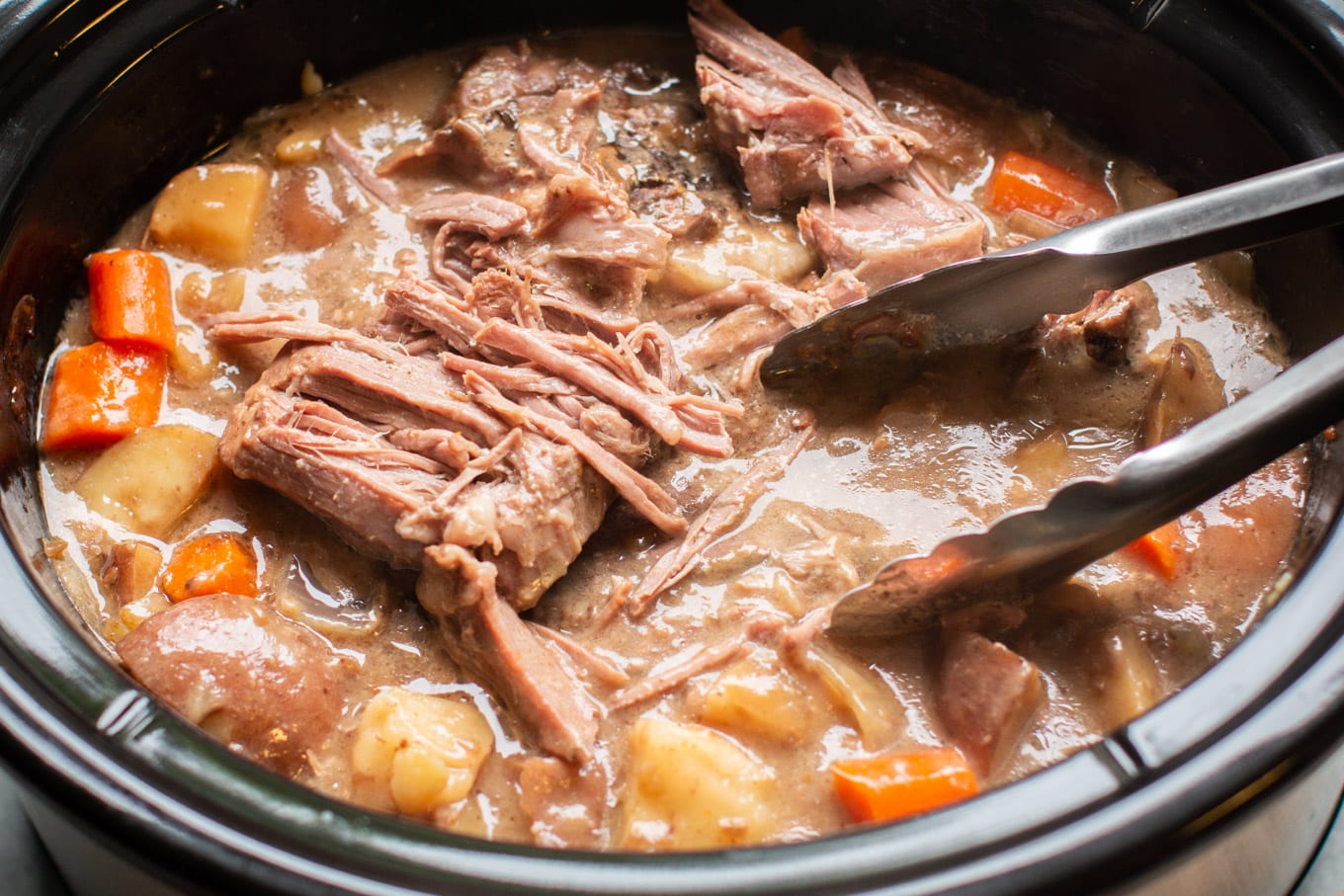 shredded pot roast with tongs in a slow cooker.