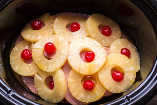 ham, pineapple rings, and maraschino cherries in black slow cooker