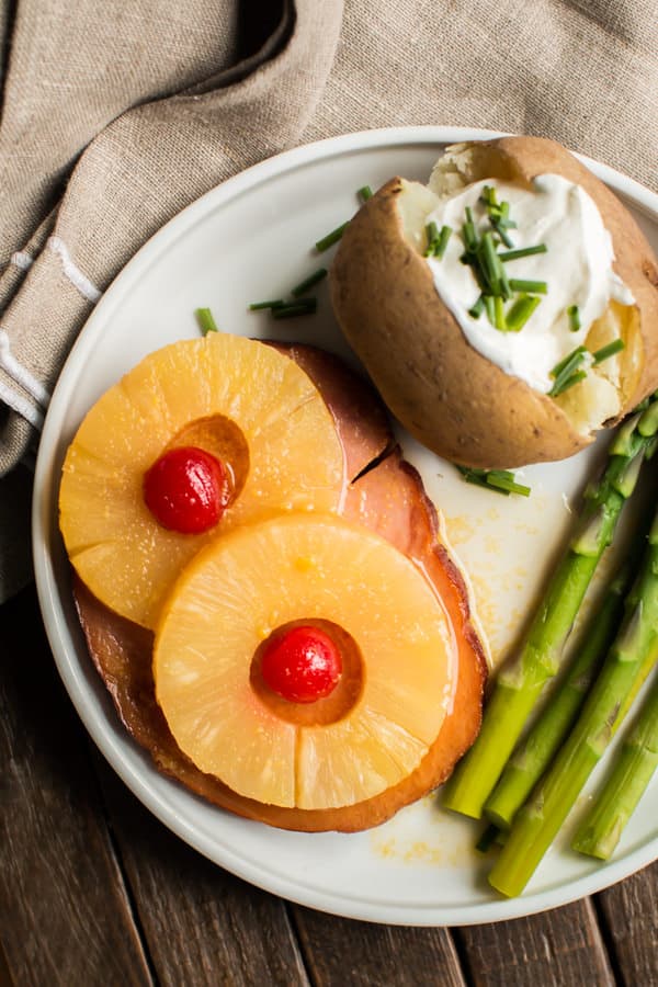 ham on plate with 2 pieces of pineapple and cherries.