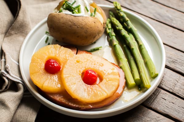 ham with pineapple, baked potato and asparagus on white plate