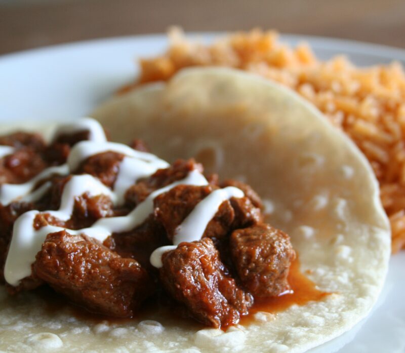 steak in sauce on tortilla with sour cream on top and spanish rice on the side.
