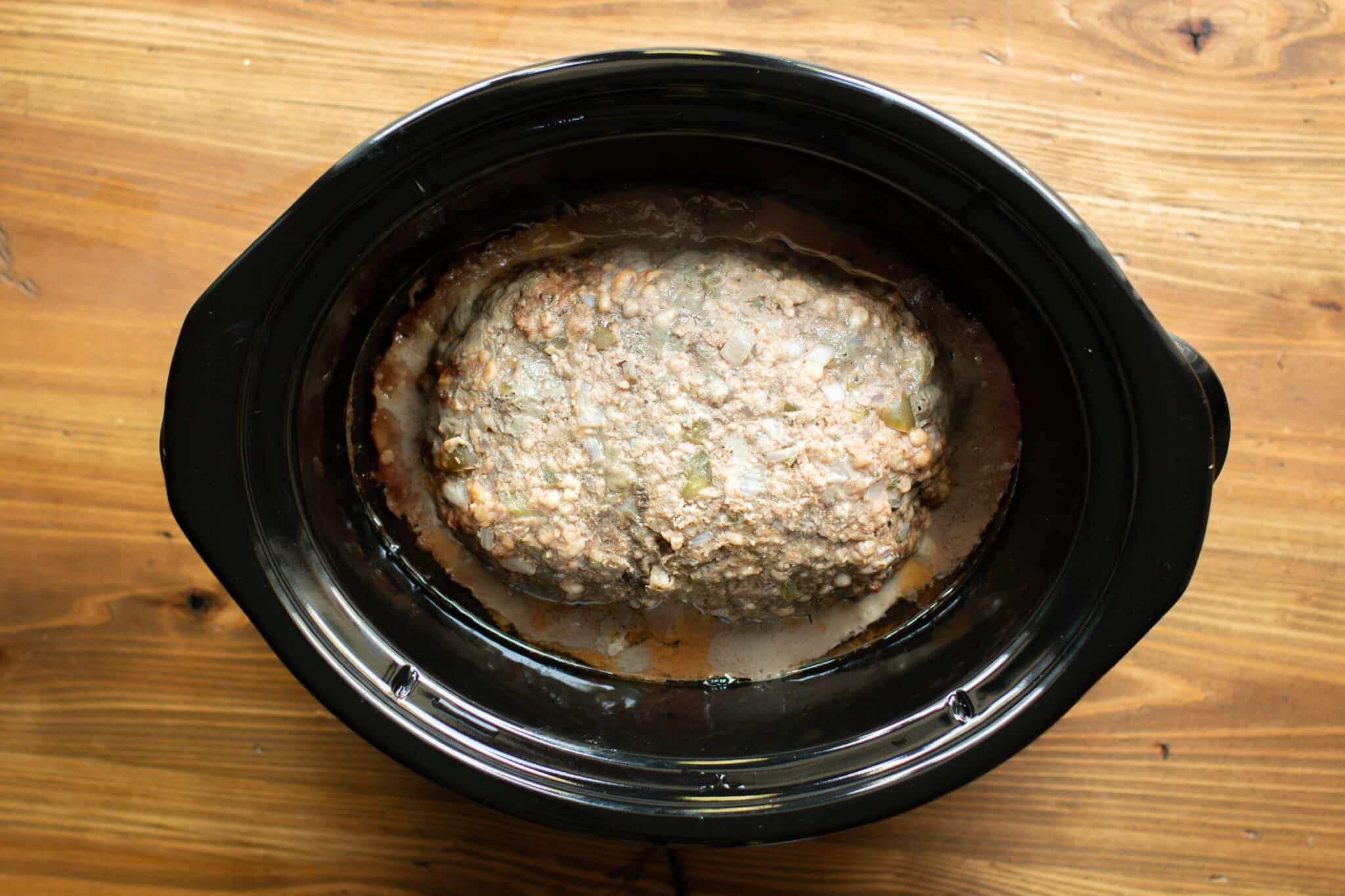 cooked meatloaf in a slow cooker with juices around the edges.