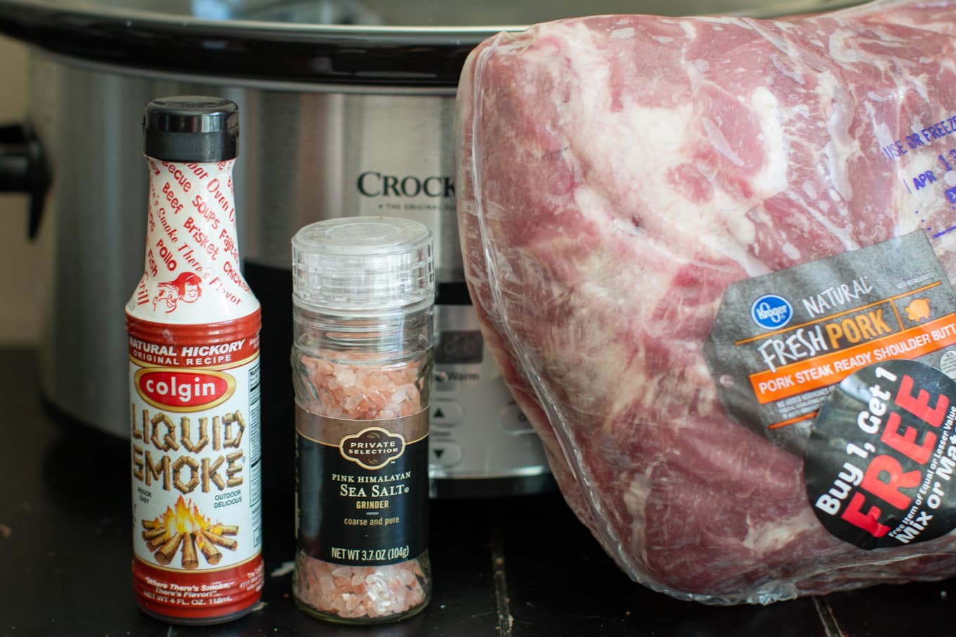 Large pork roast, Himalayan sea salt and hickory liquid smoke in front of a slow cooker.