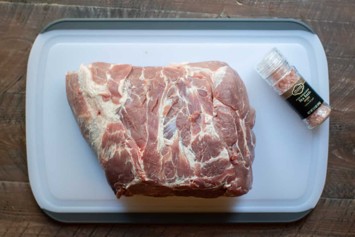 Pork roast unwrapped on a cutting board with jar of Himalayan sea salt next to it.