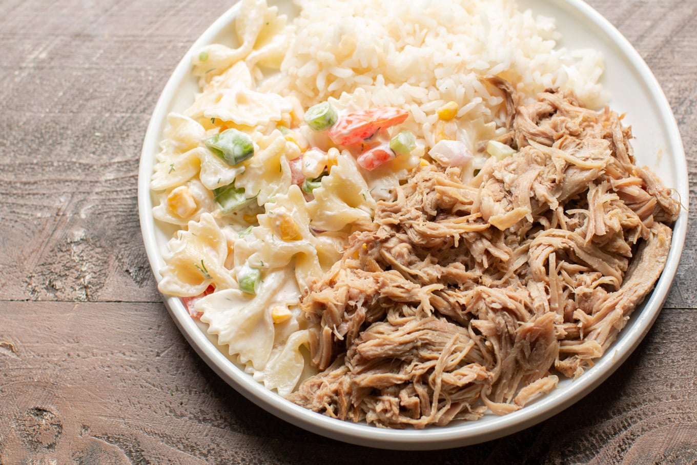 white plate with pasta salad, shredded pork and white rice.