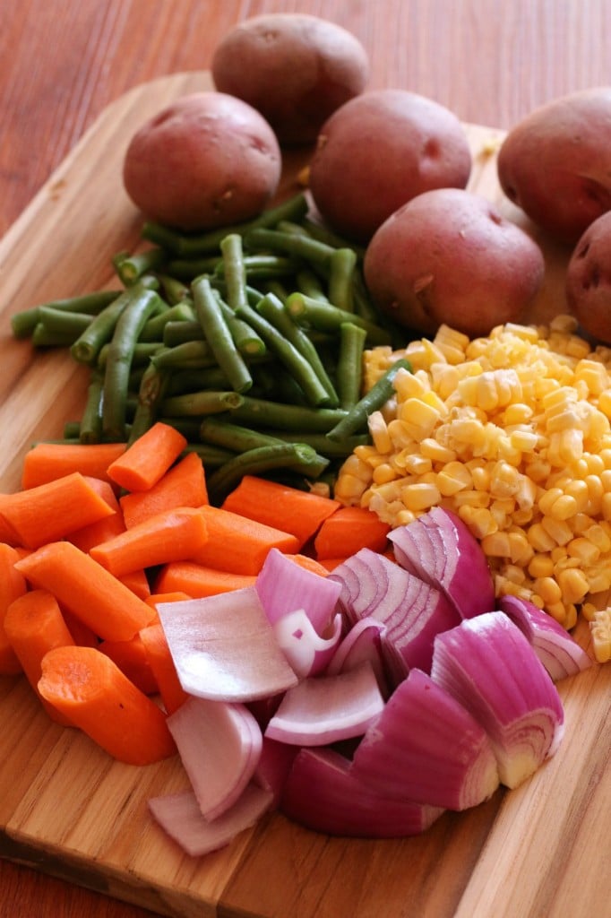 carrots, red onion, yellow corn, green beans, and red potatoes on cutting board