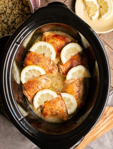 6 lemon pepper chicken thighs with lemons on top in slow cooker
