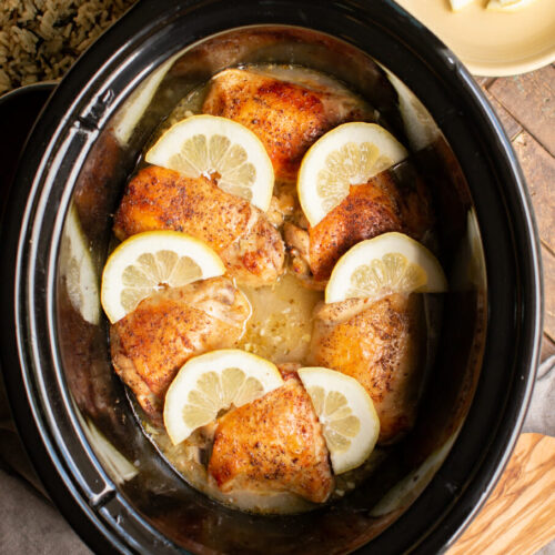 6 lemon pepper chicken thighs with lemons on top in slow cooker