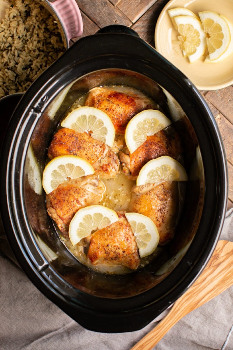 6 lemon pepper chicken thighs with lemons on top in slow cooker