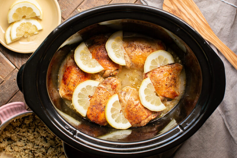 cooked lemon pepper chicken thighs in slow cooker with lemon slices on top.