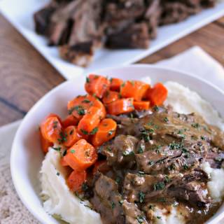 Pot roast and gravy over mashed potatoes with carrots on the side.