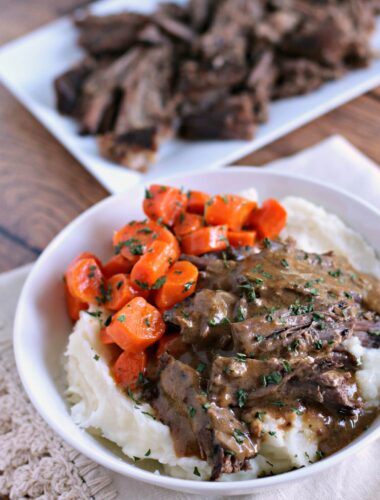 Pot roast and gravy over mashed potatoes with carrots on the side.