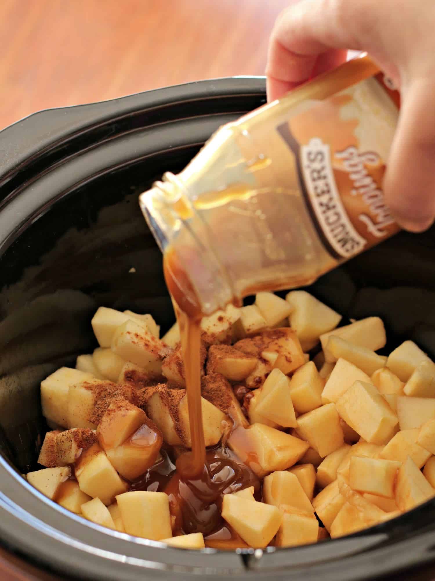 Caramel being pour over diced apples and spices in slow cooker.